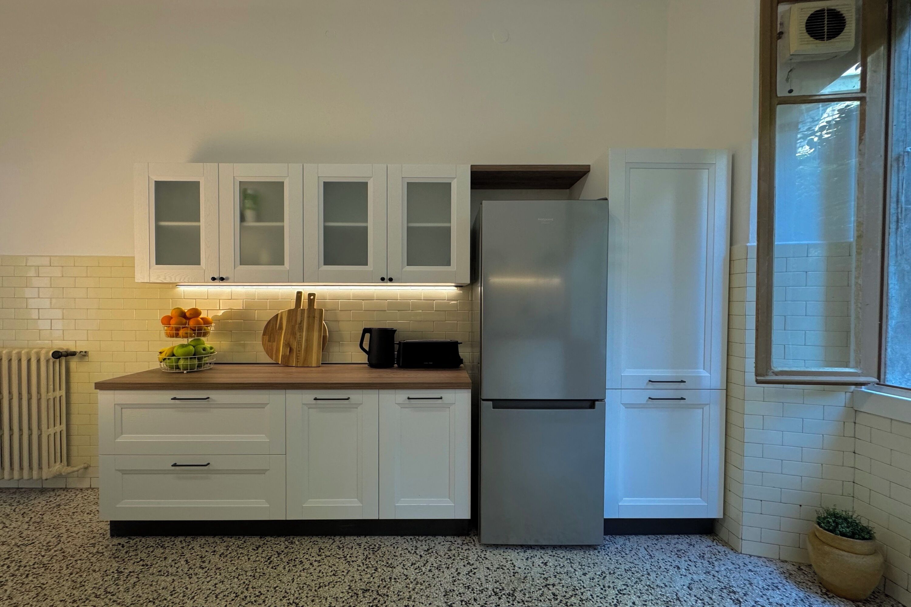 A modern kitchen with white cabinets, a stainless steel refrigerator, and a window with a view.