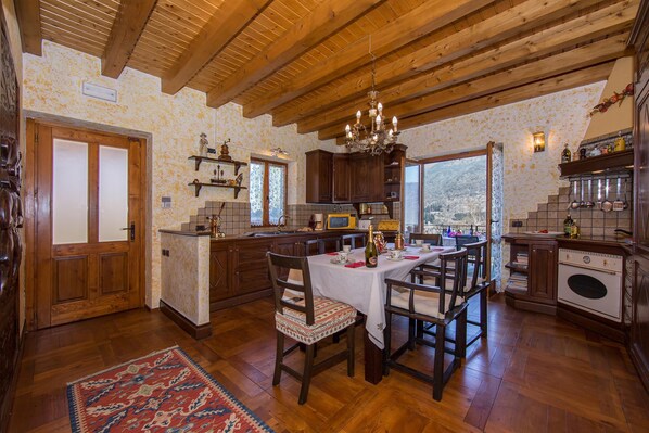 A rustic kitchen with wooden beams, a chandelier, and a dining area with a table set for two. - Villa Victoria in Macchero (Argegno)
