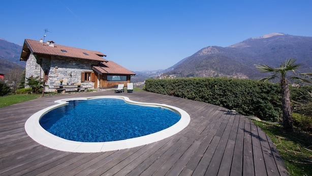 Ein Steinhaus mit Swimmingpool, Holzterrasse und Bergblick.