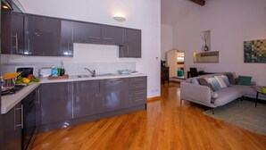 A modern kitchen with grey cabinets and a wooden floor, leading to a living area with a grey sofa and a painting on the wall. - Bella Menaggio Panoramica (Menaggio)