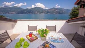 A terrace with a table set for a meal, overlooking a lake and mountains. - Bella Menaggio Panoramica (Menaggio)