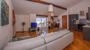 A spacious living area with a large sofa, a television, and a dining area with chairs. - Bella Menaggio Panoramica (Menaggio)