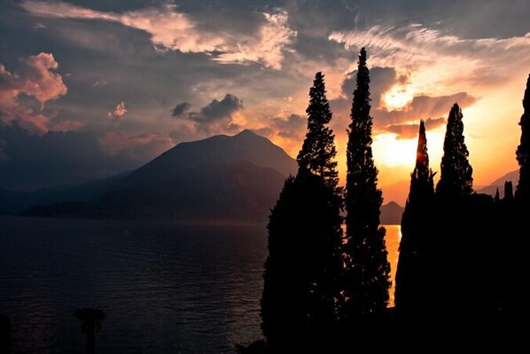 La silhouette d’une montagne au coucher du soleil, avec un lac et de grands arbres au premier plan.