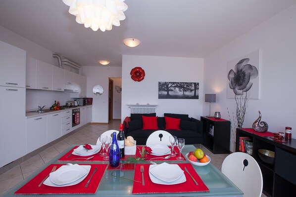 Un salon moderne avec un coin repas aménagé pour un repas, comprenant une table en verre, des sets de table rouges et un arrangement floral rouge en guise de centre de table.