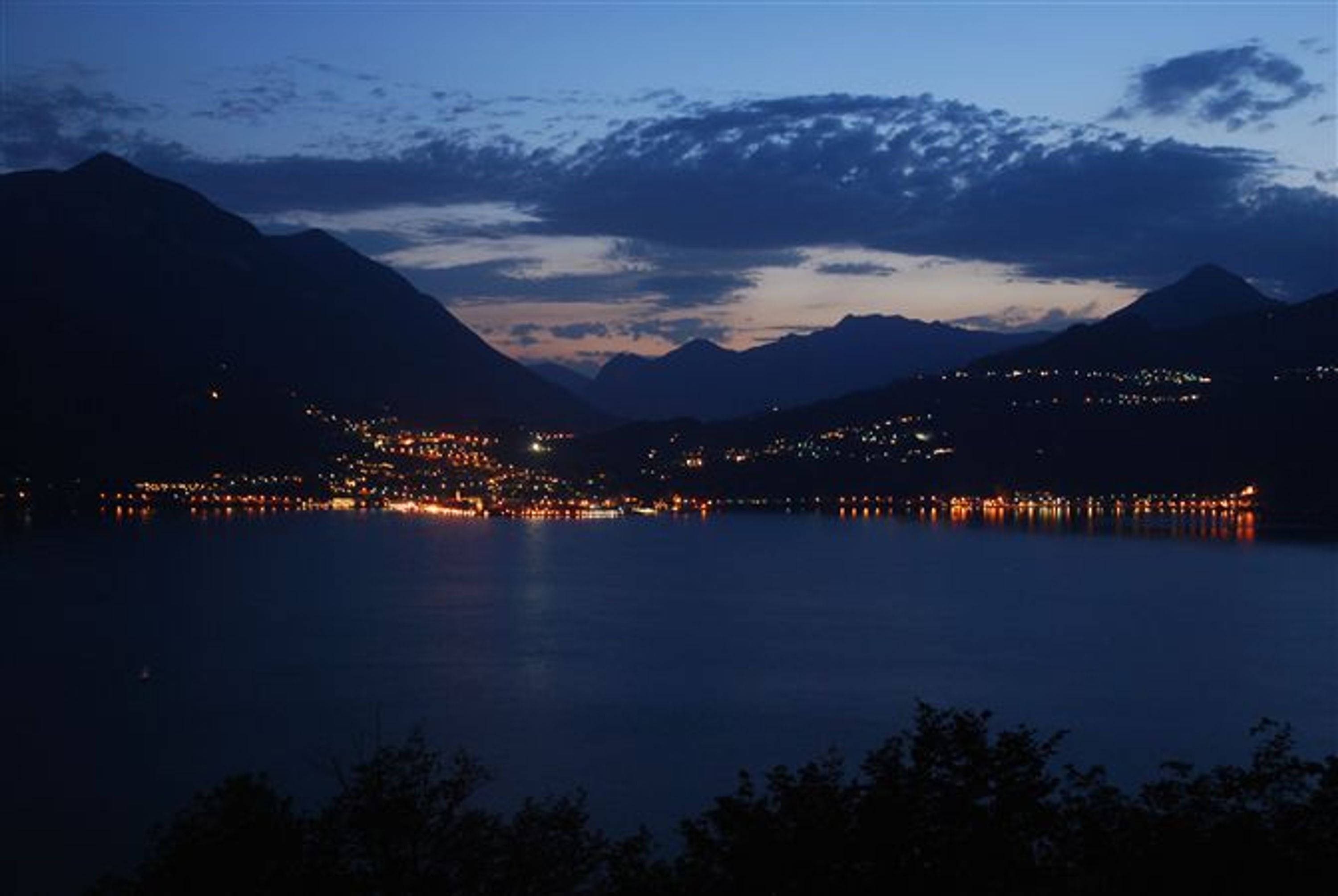 A nighttime view of a lake with surrounding mountains and a town with illuminated buildings.