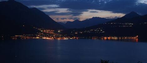 A nighttime view of a lake with surrounding mountains and a town with illuminated buildings.