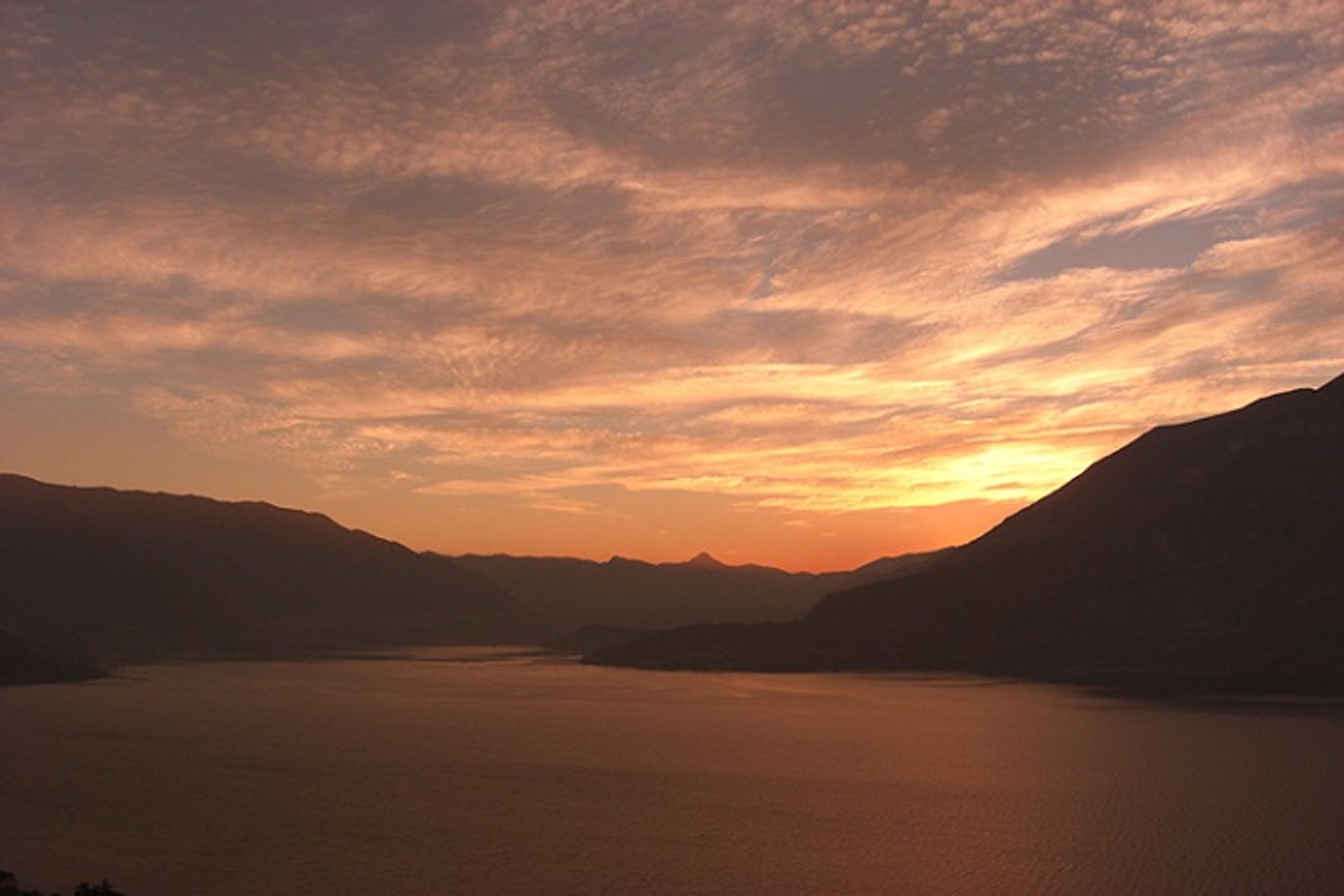 Ein friedlicher Sonnenuntergang über einem stillen See, umgeben von Bergen.