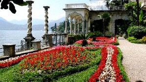 Un jardín con un sendero que lleva a un edificio de columnas y vista al agua.