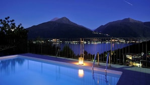 Une piscine avec vue sur les montagnes et un lac, de nuit.