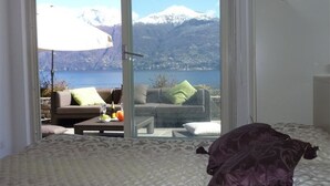A bedroom with a bed, a sofa, and a view of a lake and mountains. - Villa Panoramica in Menaggio (Plesio)