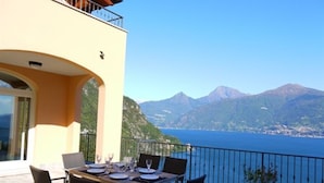 A terrace with a table set for dining, overlooking a body of water and mountains. - Villa Panoramica in Menaggio (Plesio)