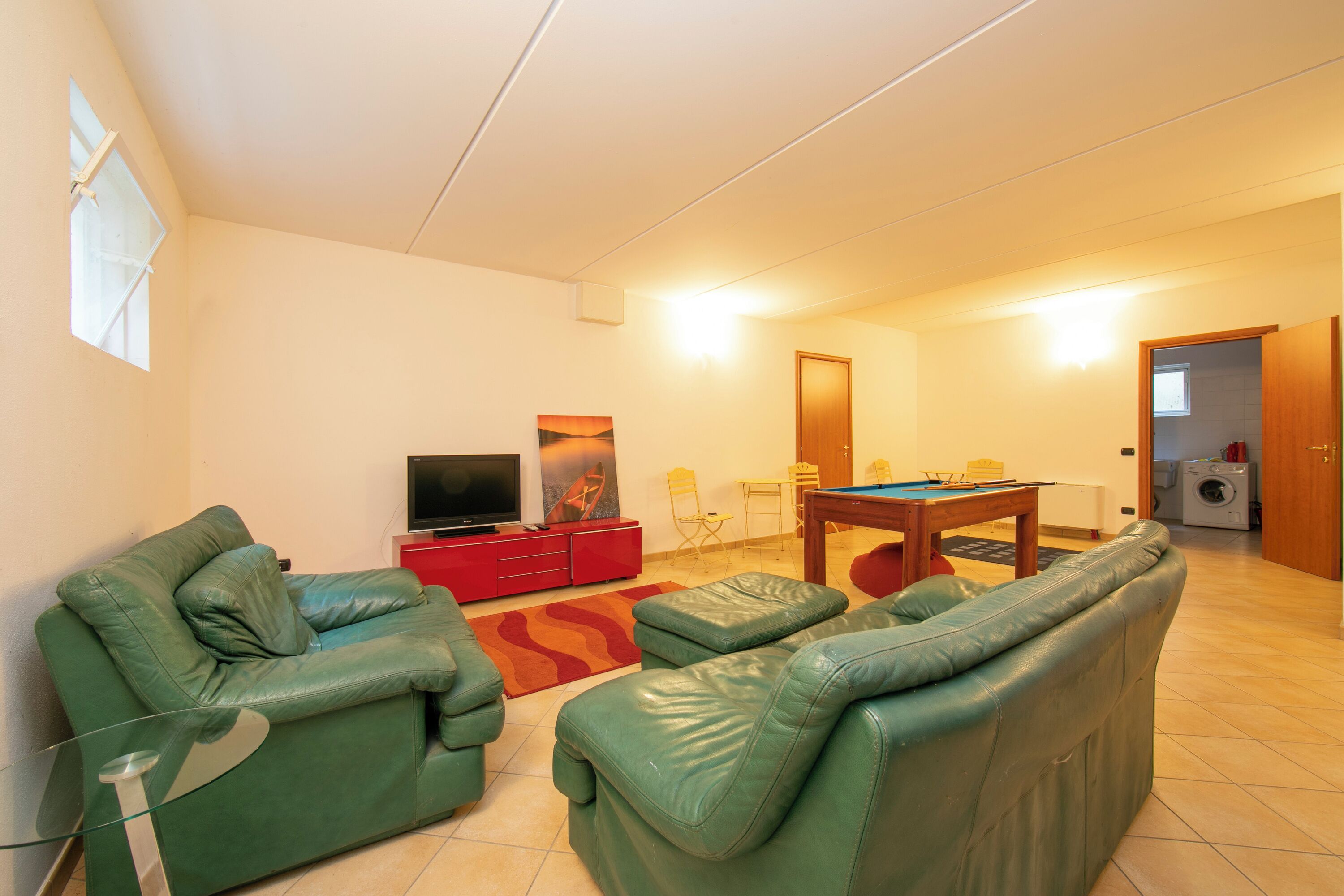 A living room with green leather sofas, a red entertainment unit, a pool table, and a television.