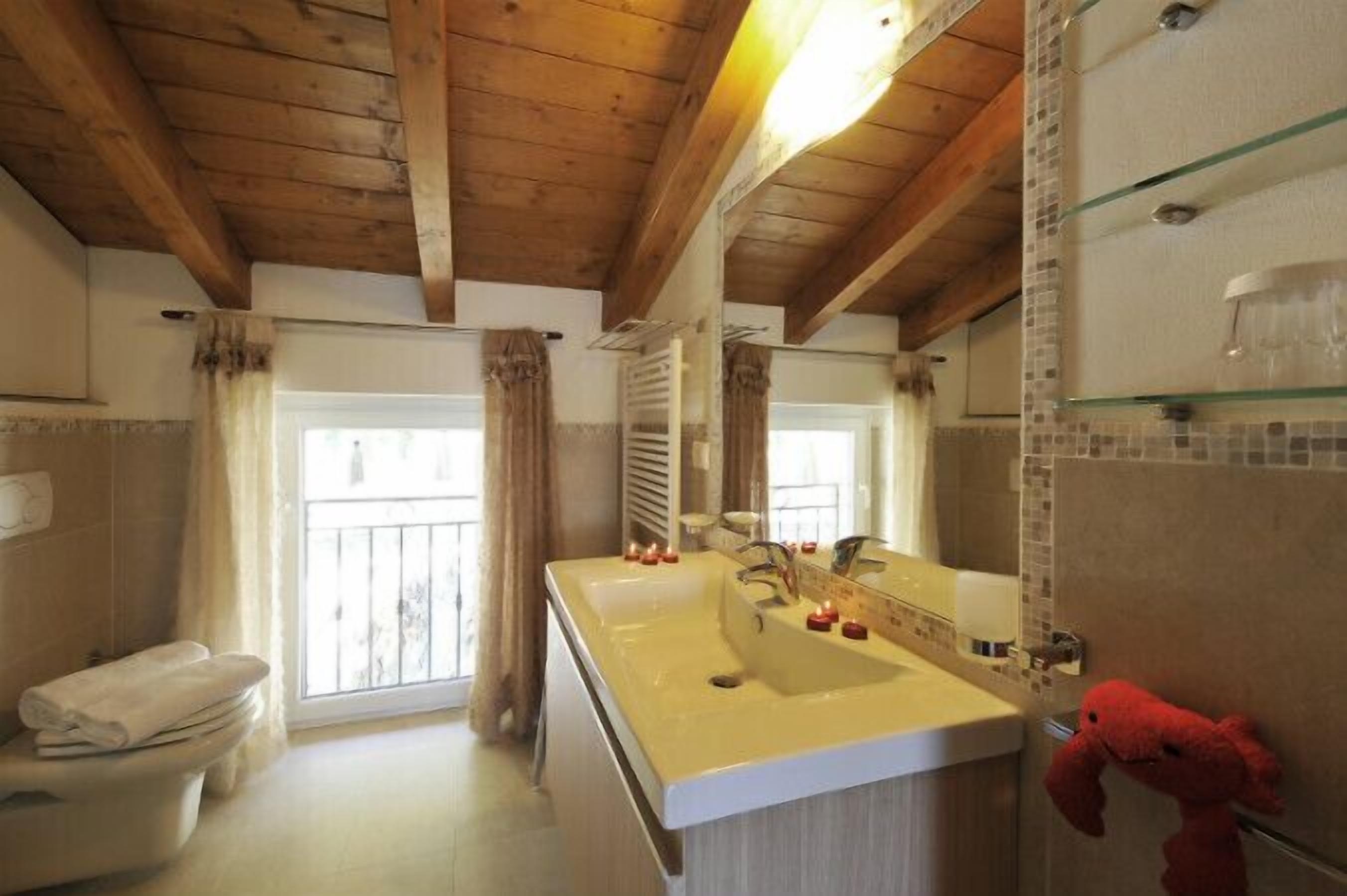 A bathroom with wooden beams, a large mirror, a double sink, and a toilet.