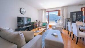 A modern living room with a flat-screen TV, sofas, a coffee table, and a dining area with chairs. - Bella Menaggio Terrazzo (Menaggio)