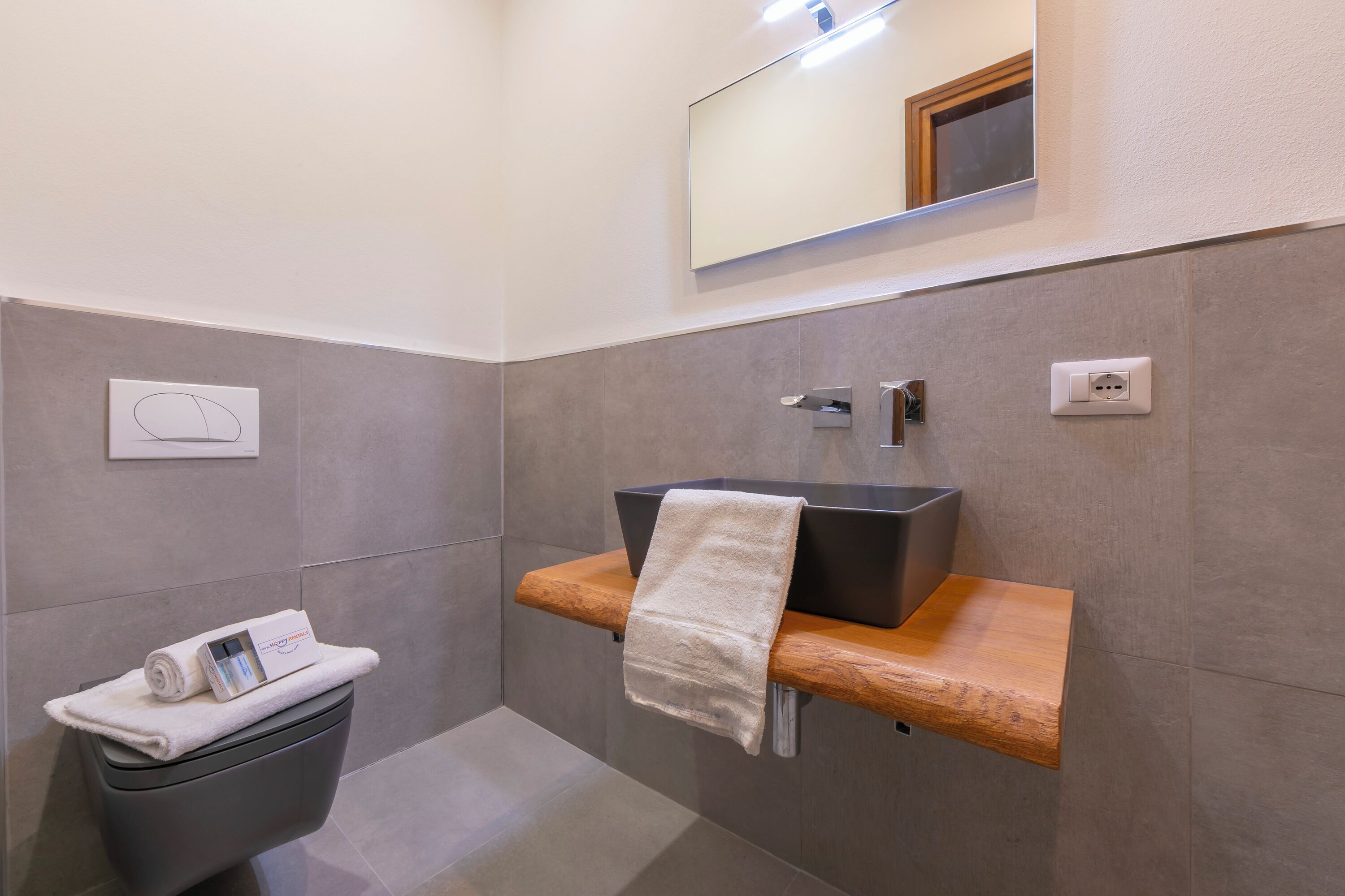 A modern bathroom with a dark sink, wooden countertop, and a towel on the toilet.