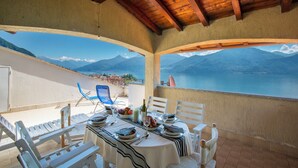 A terrace with a table set for dining, overlooking a mountainous landscape and a body of water. - Bella Menaggio Terrazzo (Menaggio)