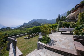 Eine Steinterrasse mit Gartenmöbeln, eine Steinmauer und Blick auf Berge.
