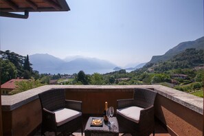 A balcony with wicker furniture, a bottle of champagne, and a glass. The balcony overlooks a scenic view of mountains and a lake. - Villa Lakecomo - Ritrovo (Menaggio)
