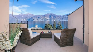 A balcony with wicker furniture, a vase of white flowers, and a view of mountains and a lake. - Bellavista Grande in Menaggio (Menaggio)