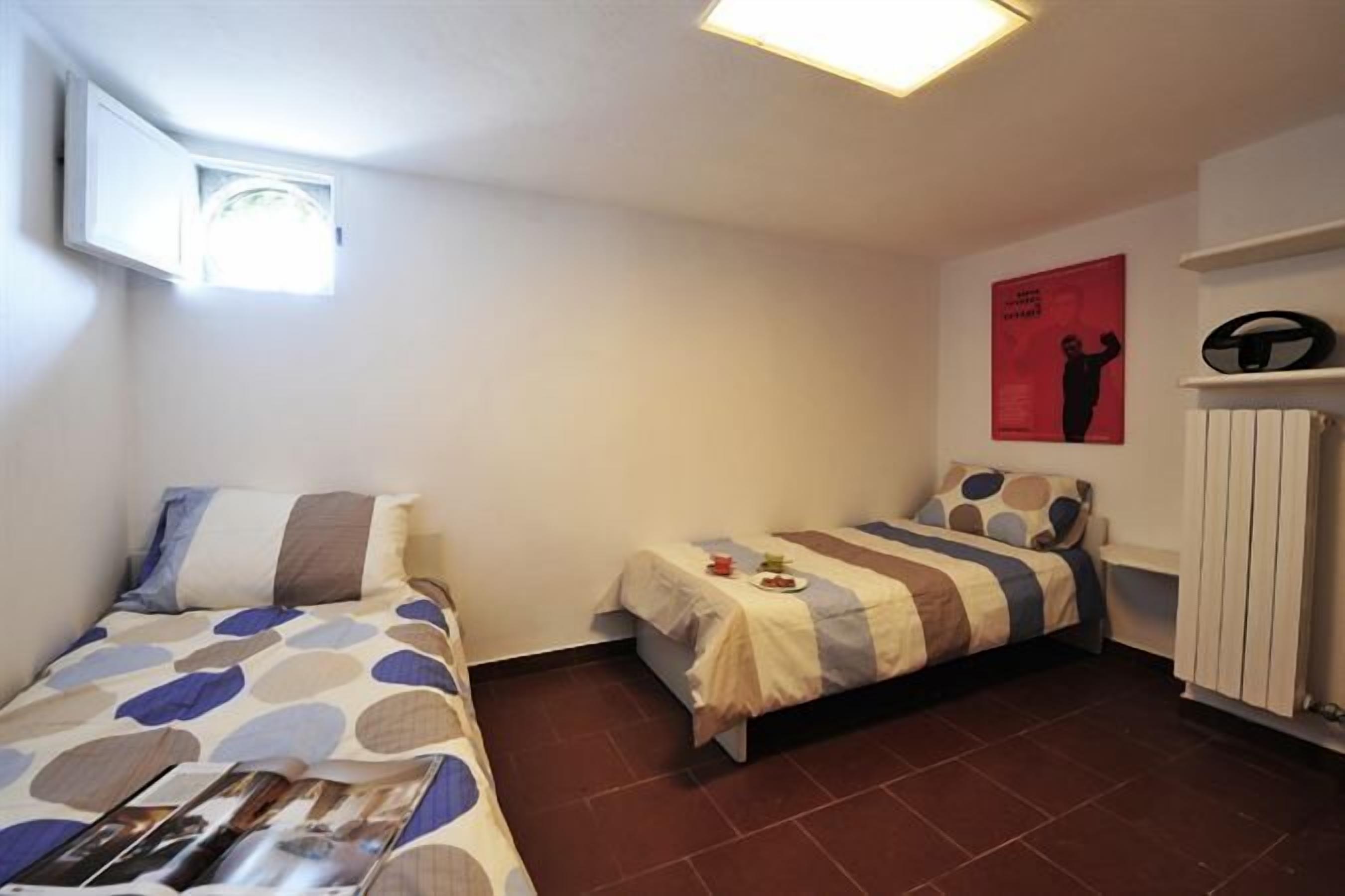 A small, well-lit room with two beds, a radiator, and a poster on the wall.