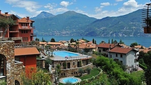 Un resort con piscina, edificios de piedra y vistas a montañas y un lago.