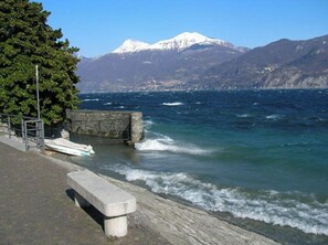 A coastal walkway with a bench, a stone wall, and a boat dock. - La Perla Di Sonenga - Giardino (Menaggio)