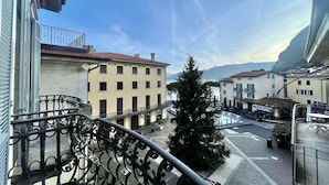 A balcony with wrought iron railings overlooking a street with buildings, a tree, and a clear sky. - Menaggio Fantastico in Menaggio (Menaggio)