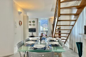 A dining area with a glass table set for six, a wooden staircase, and a view of the mountains through the window. - Menaggio Fantastico in Menaggio (Menaggio)