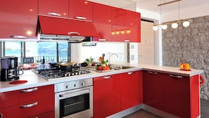 A modern kitchen with red cabinets, stainless steel appliances, and a stone accent wall. - Villa Bianca - Grande (Menaggio)