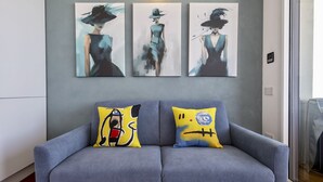 Un sofá gris con dos almohadones coloridos, una pared gris y tres cuadros abstractos encima.