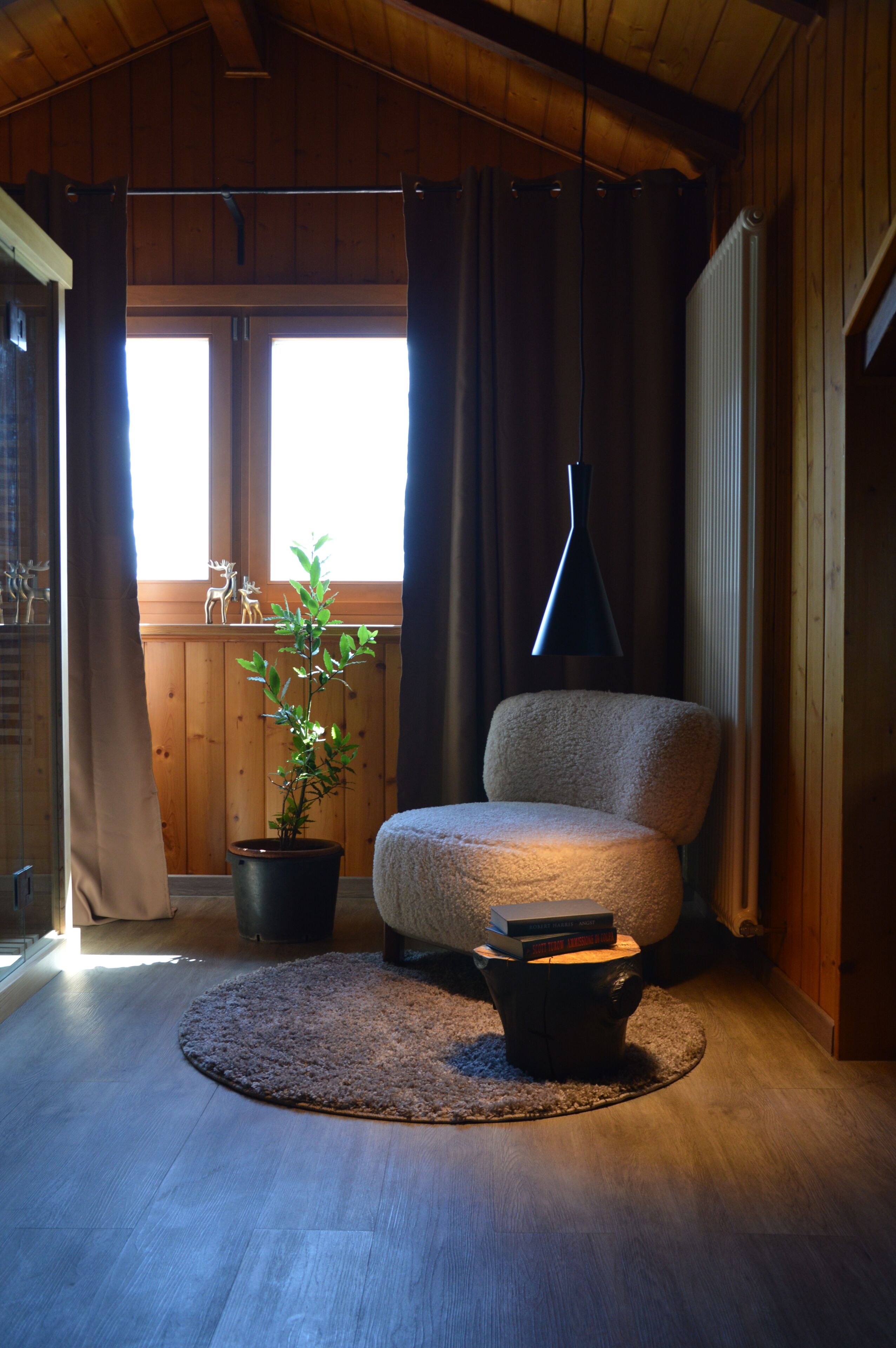 Ein gemütliches Zimmer mit Holzboden, einem runden Teppich, einem Sessel, einer Topfpflanze und einem fenster mit Vorhängen.