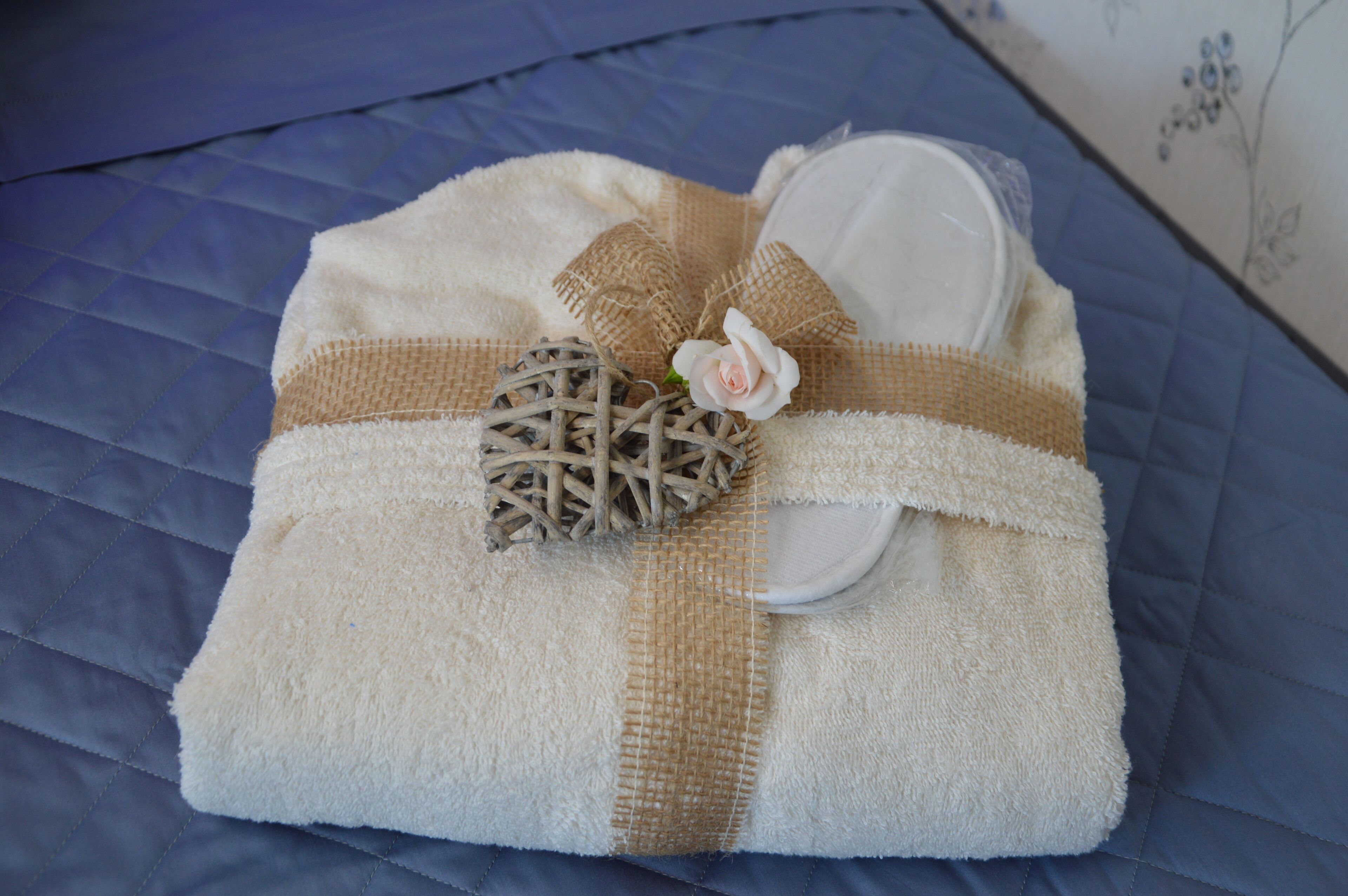 A neatly folded towel with a burlap bow and a small decorative item on a blue quilted bedspread.