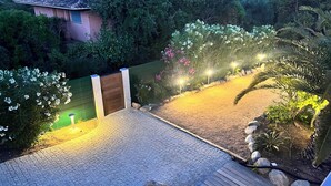 Ein gepflasterter Patio-Bereich mit einer Holzterrasse, umgeben von einem grünen Zaun und verschiedenen Pflanzen.