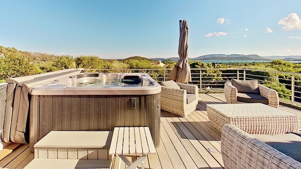 Ein Whirlpool auf einer Holzterrasse mit Korbmöbeln und Blick auf die Landschaft.