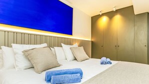 A hotel room with a large bed, a headboard with built-in lighting, a wardrobe, and a blue wall.