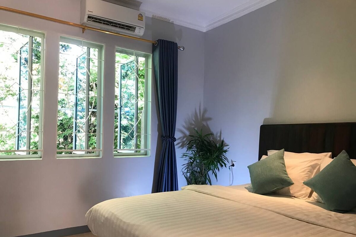 Ein Schlafzimmer mit einem Bett, einer Topfpflanze und einem Fenster mit Vorhängen.