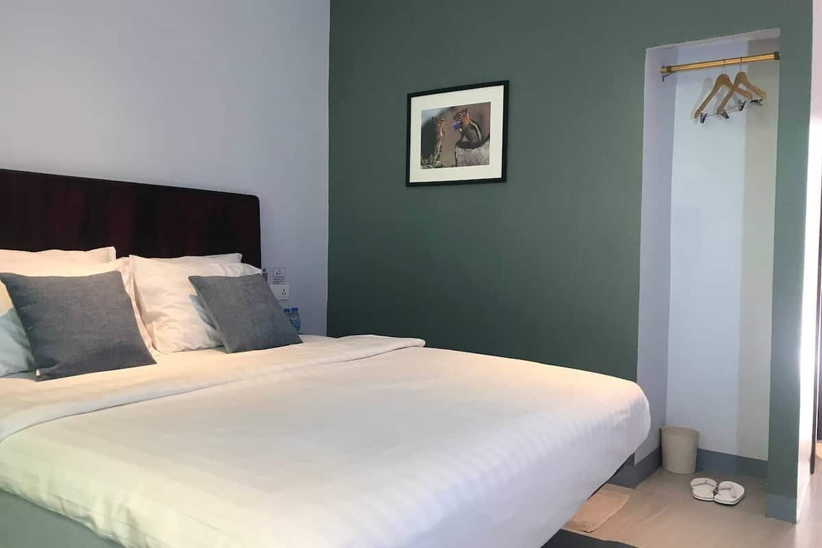 Una cama bien hecha con ropa de cama blanca y gris, un cuadro en la pared y un perchero con ganchos.