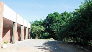 Un bâtiment à la façade en briques, avec une allée de gravier menant à un espace abrité agrémenté de rideaux verts.