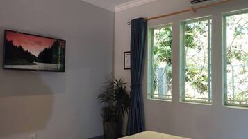 A bedroom with a bed, a potted plant, a picture on the wall, and a window with curtains.