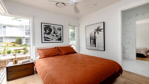 Une chambre avec un grand lit, une table de chevet et une fenêtre avec des stores. Deux tableaux encadrés sont accrochés au mur.