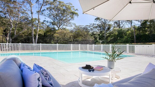 Un espace aménagé au bord de la piscine, avec une clôture blanche, une piscine et un fauteuil de relaxation agrémenté de coussins.
