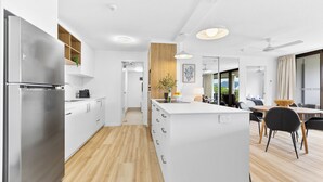Eine moderne Küche mit weißen Schränken, einem Edelstahl-Kühlschrank, einer Wand mit Holzvertäfelung und einem Essbereich mit Tisch und Stühlen.