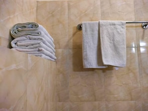 A bathroom with a marble floor, a towel rack with two towels, and a stack of folded towels on the floor.