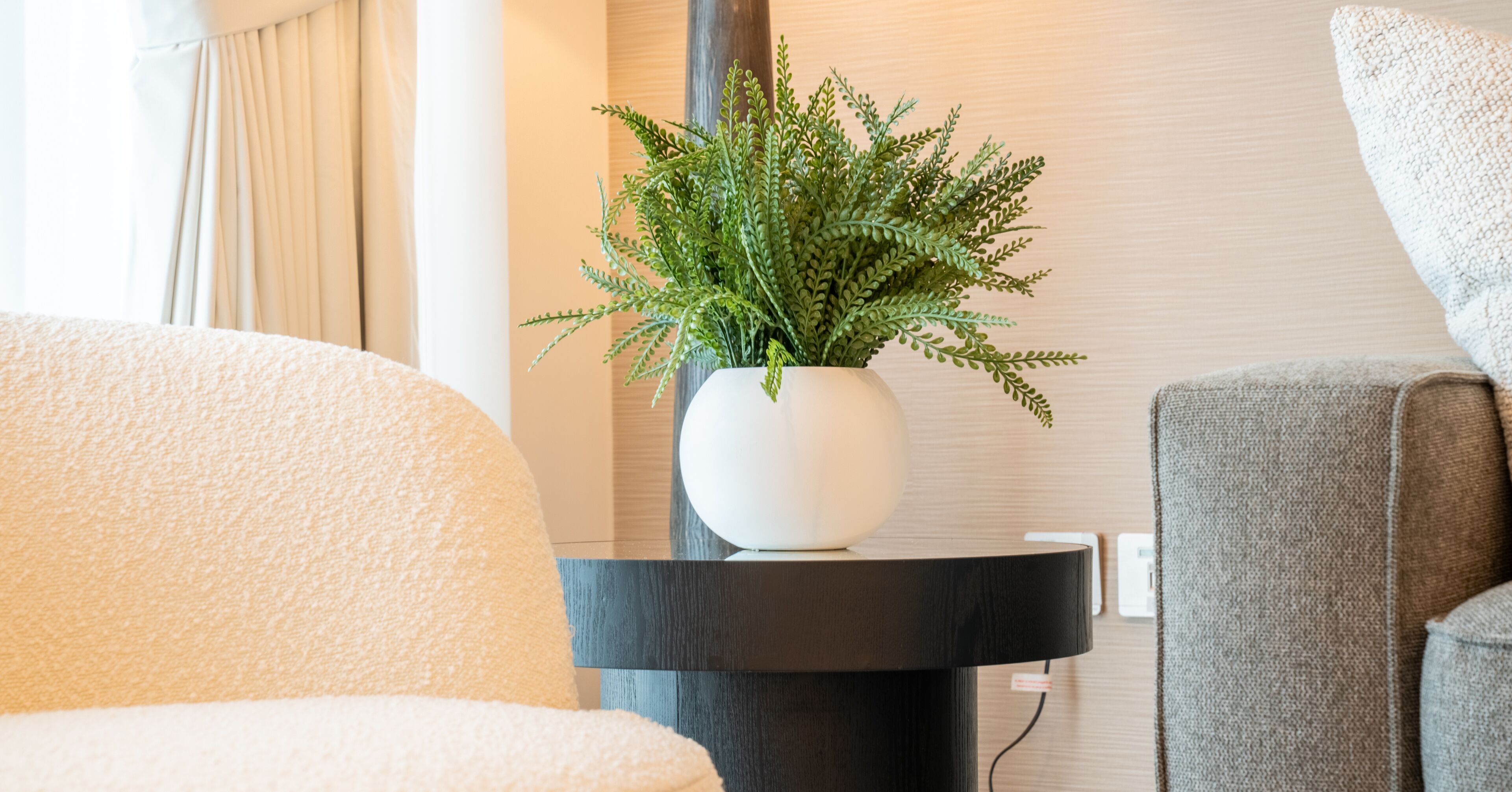 A modern living room with a round black side table holding a white vase with green foliage.