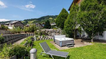 Un jardín con un jacuzzi, sillas de descanso y un muro de piedra.