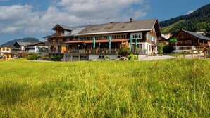 A hotel with multiple balconies, a grassy field in the foreground, and a mountainous backdrop.