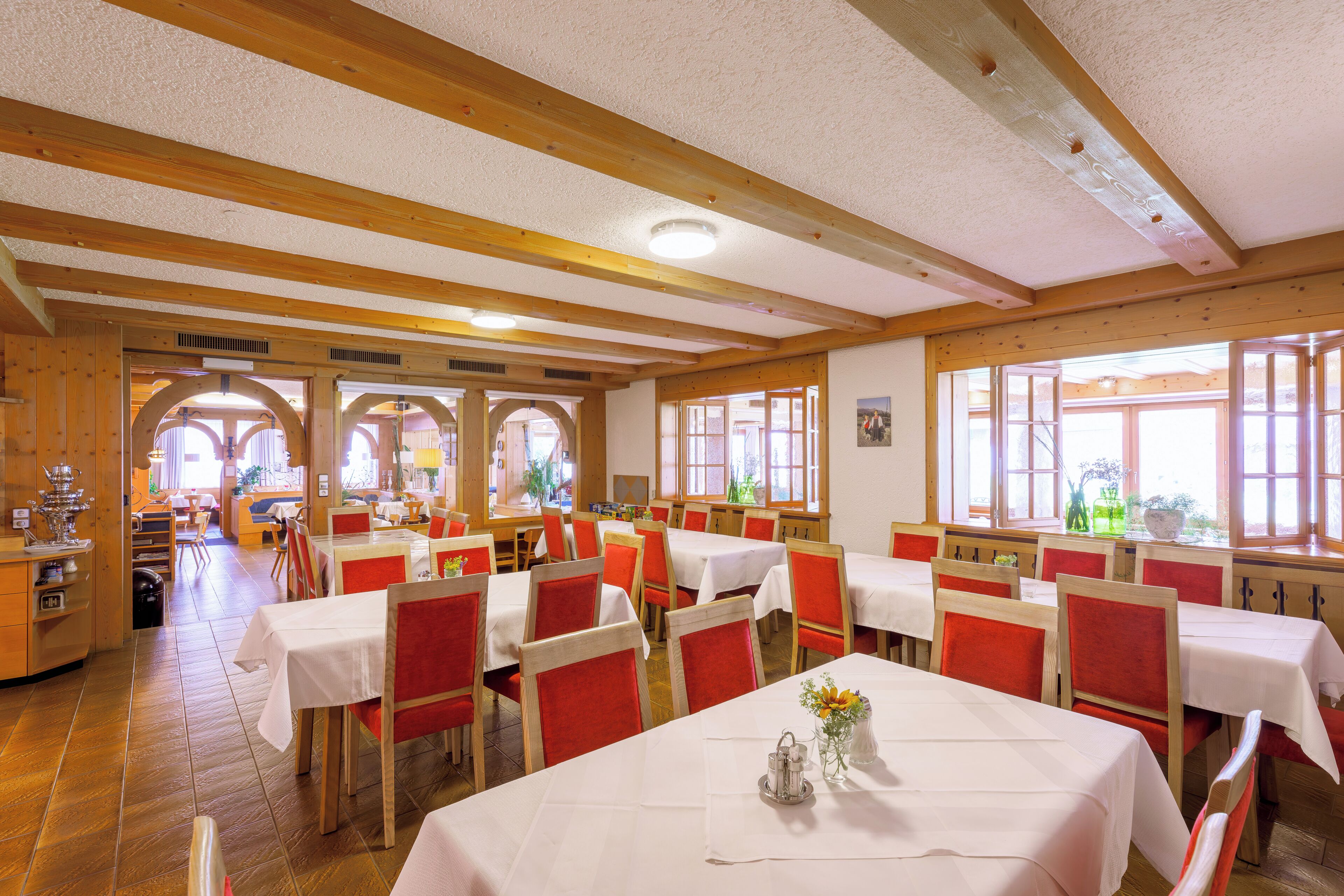 A restaurant with wooden beams, white tablecloths, and red chairs.