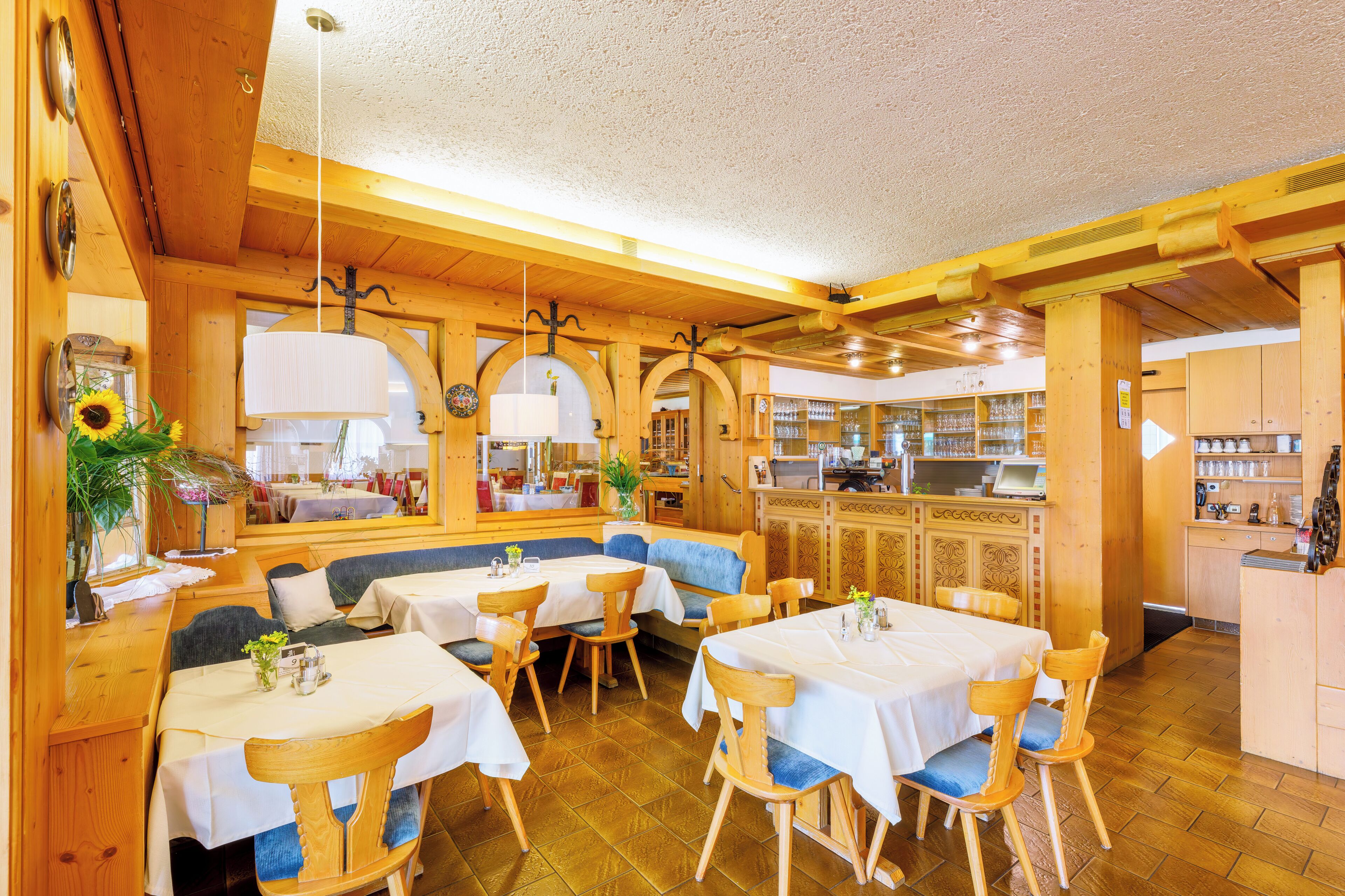 Un restaurant au décor intérieur en bois, avec des tables recouvertes de nappes blanches et des sièges rembourrés de tissu bleu.