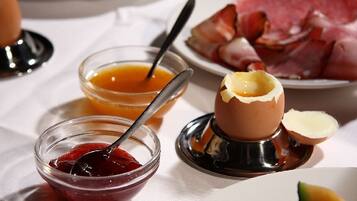 Desayuno con un plato de jamón, un huevo duro y dos recipientes pequeños con mermelada y salsa.