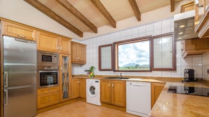 Cucina con mobili in legno, elettrodomestici in acciaio inox, lavatrice e un'ampia finestra con vista.
